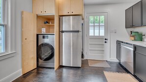 A compact kitchen with a built-in washer and dryer, wooden cabinets, and a stainless steel refrigerator.