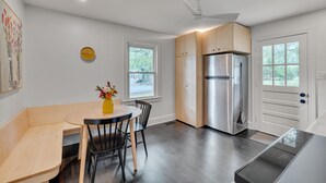 A modern kitchen with a built-in refrigerator, wooden cabinets, a dining area with a round table and chairs, and a window providing natural light.