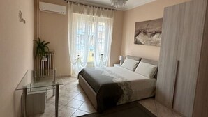 Een slaapkamer met een bed, nachtkastje, glazen scheidingswand, raam met gordijnen en een schilderij aan de muur.