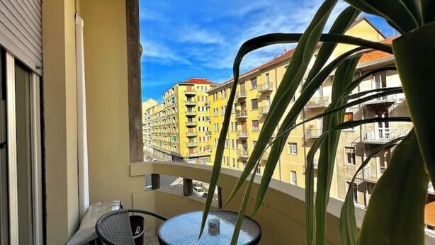 Een balkon met een ronde tafel en stoelen, met uitzicht op een geel gebouw met balkons.