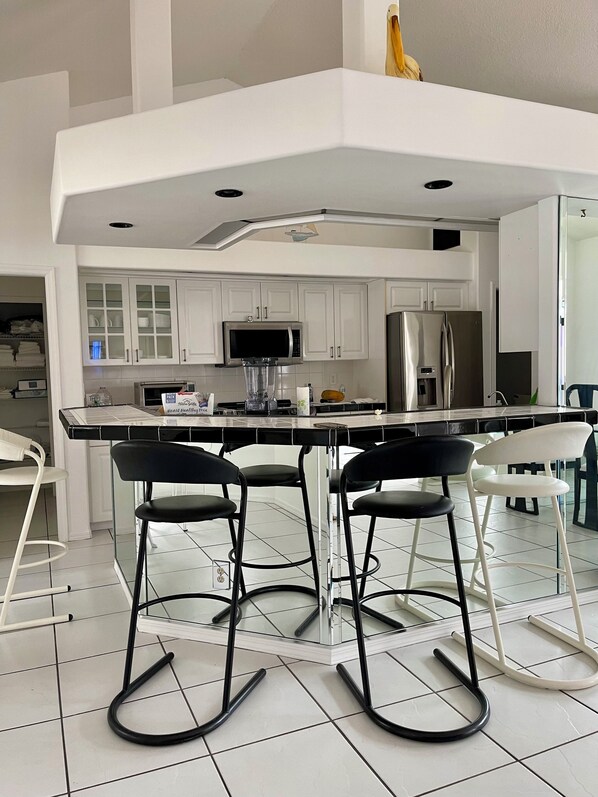 A modern kitchen with white cabinets, a stainless steel refrigerator, a microwave, and a bar area with stools.
