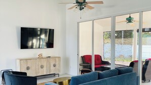 A modern living room with a blue sofa, a flat-screen TV, and a ceiling fan. - Charming 3-bedroom villa with AC and WiFi in lovely Sebastian (Sebastian)