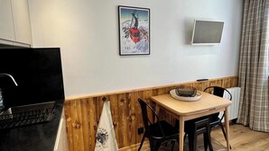 A modern kitchen with a wooden accent wall, a dining area with a table and chairs, a mounted TV, and a painting on the wall.