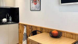 A modern kitchen with white cabinets, a black countertop, and a wooden dining table with black chairs. A framed picture hangs on the wall above the table.