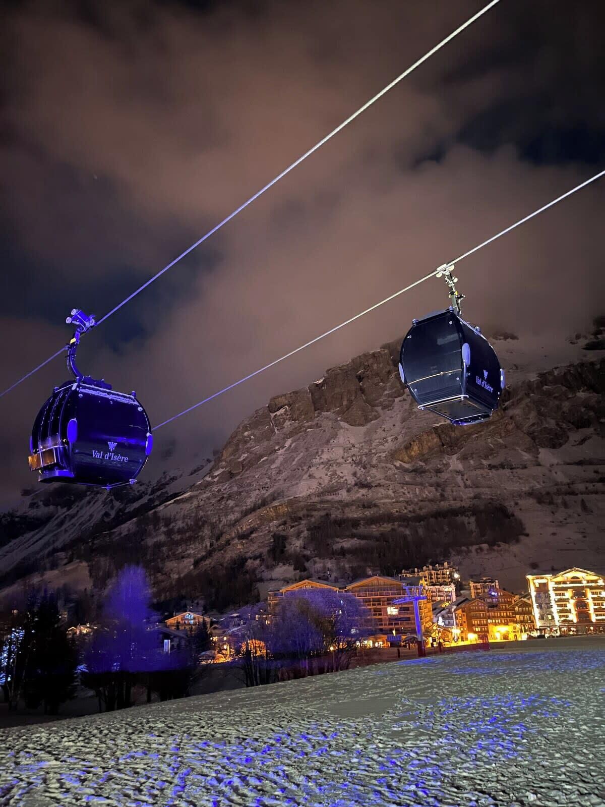 A cable car system with illuminated gondolas against a mountainous backdrop.