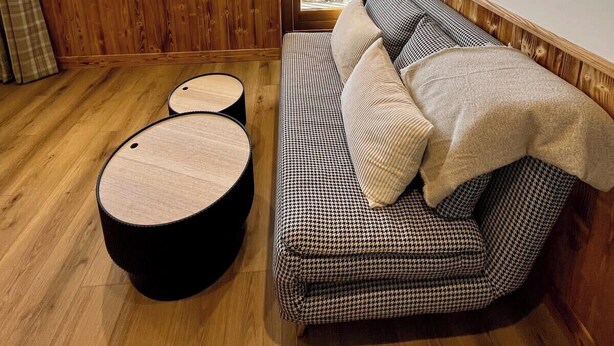 A cozy room with a houndstooth sofa, a round ottoman, and a view of a ski resort.