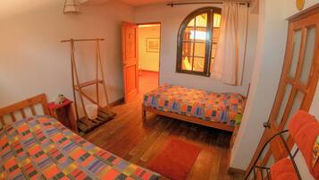 A cozy room with two beds, a wooden ladder, a window with curtains, and a door with a wooden frame.