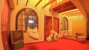 Una stanza con tappeto rosso, travi in legno, una poltrona sospesa, televisore e mobili in vimini.
