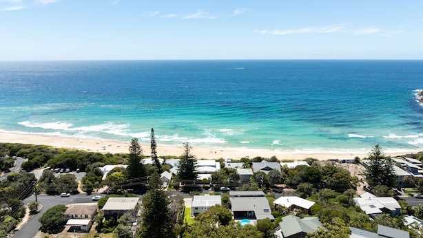 A coastal residential area with houses, a beach, and a clear view of the ocean.
