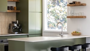 A kitchen with a large island, bar stools, a coffee machine, and wooden shelves.