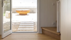 An open door leading to a balcony with a wooden floor, a white wall, and a small wooden bench.