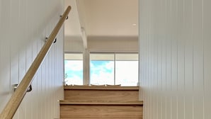 A wooden staircase with white paneling on the walls, leading to a room with a view of the sky.