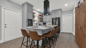 Una cocina moderna con una isla central, taburetes de bar y una campana extractora negra grande.