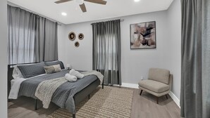 Un dormitorio con cama, una silla, un ventilador de techo y una pared con un cuadro y tres elementos decorativos circulares.
