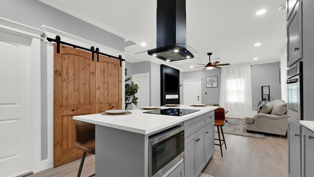 Una cocina moderna con una isla central, horno empotrado y una puerta corredera de madera.