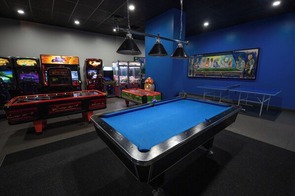 Une salle de billard équipée d’une table de billard, de jeux d’arcade et ornée d’une fresque murale.