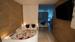 Een moderne badkamer met een ruime badkuip vol rozenblaadjes, een flatscreen televisie aan de muur en een inloopdouche.