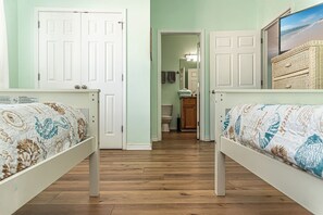 Two single beds with matching headboards and footboards, a large window offering a beach view, and a door to a bathroom with a toilet and sink.