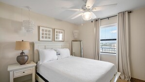 A neatly arranged bedroom with a bed, bedside table, lamp, ceiling fan, and window with curtains. - Lei Lani 703 (Orange Beach)