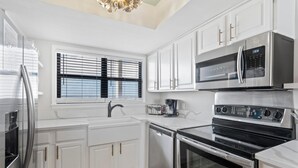 A modern kitchen with white cabinetry, stainless steel appliances, and a window with blinds. - Lei Lani 703 (Orange Beach)