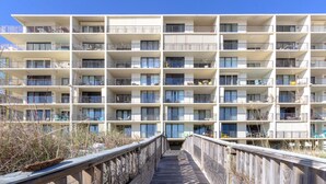 A multi-story hotel with balconies, a wooden walkway, and a clear blue sky. - Lei Lani 703 (Orange Beach)