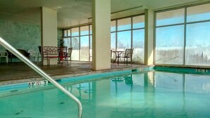 An indoor swimming pool with clear glass walls, a poolside seating area, and a view of a snowy landscape. - Lei Lani 703 (Orange Beach)