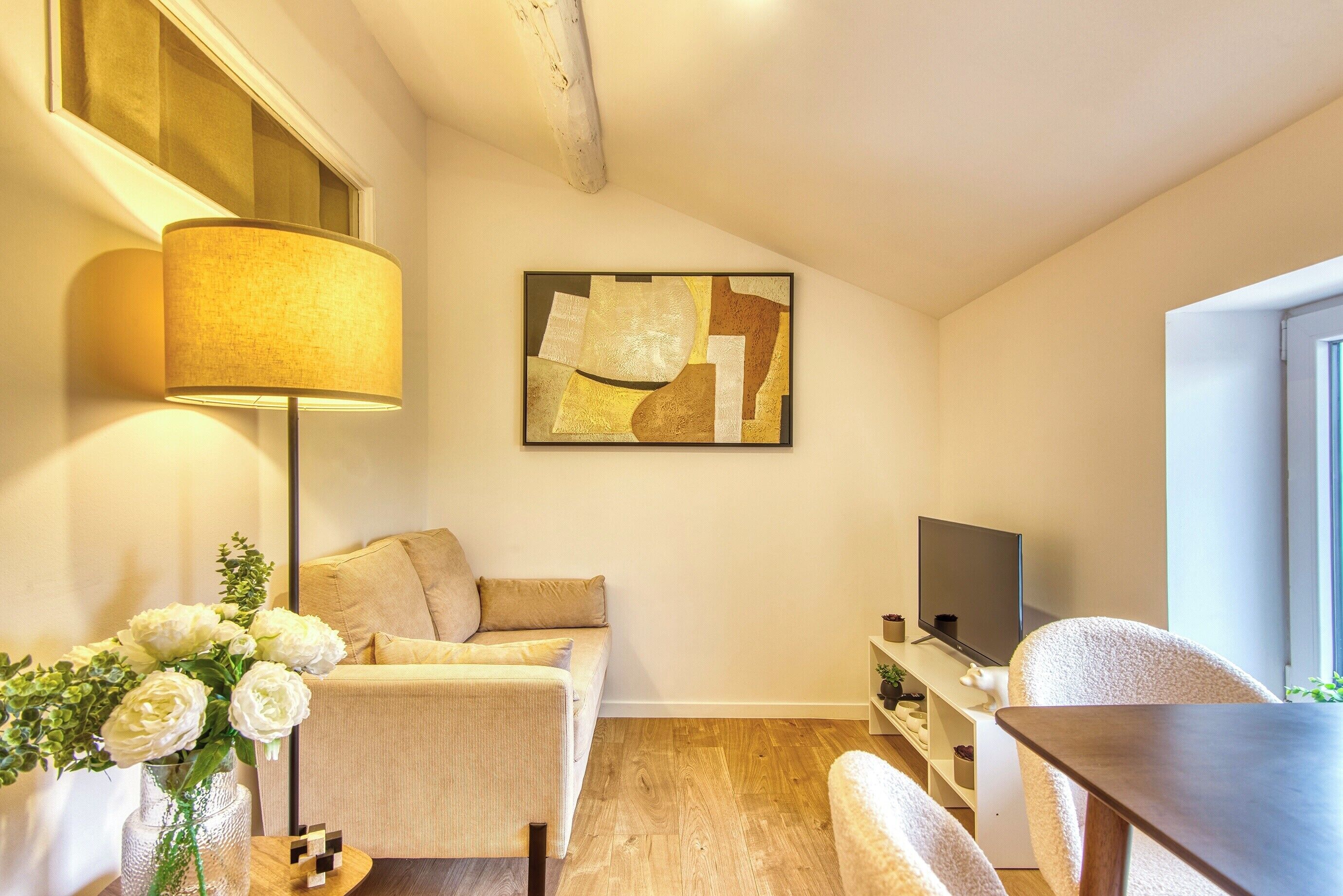 Un salon moderne avec un canapé, un téléviseur, une lampe et un tableau accroché au mur.
