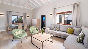 Een ruime woonkamer met een hoge nok, een zithoek, een eethoek en uitzicht op buiten.