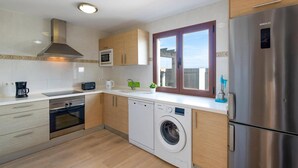 Een moderne keuken met een roestvrijstalen koelkast, een inbouwoven, een magnetron, een wasmachine en houten kastjes.
