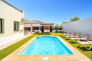 Une piscine avec un espace patio, des chaises longues et un coin salon abrité.