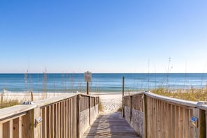 A wooden boardwalk leading to a sandy beach with a clear blue sky. - Lei Lani 706 (Orange Beach)