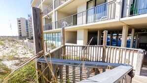 Ein mehrstöckiges Gebäude mit Balkonen, einer Holzterrasse und einem Sandstrand im Hintergrund.