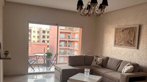 Een moderne woonkamer met een grote hoekbank, een salontafel en een kroonluchter. Er is een schuifdeur naar een buitenruimte met een tafel en stoelen.