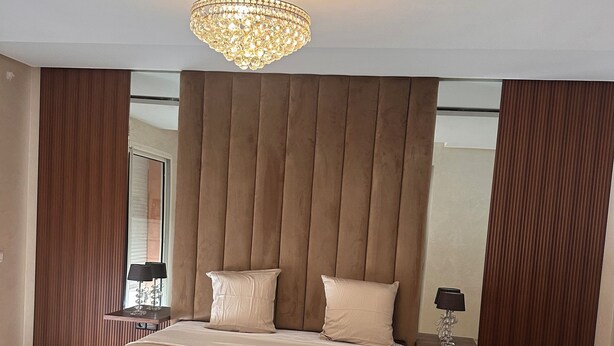 Een slaapkamer met een groot bed, een kroonluchter en een nachtkastje met een lamp.