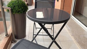 Een balkon met een ronde tafel, twee stoelen, een potplant en uitzicht op een gebouw met balkons.