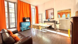 Un salon avec un canapé, un téléviseur, une table à manger et des rideaux orange.