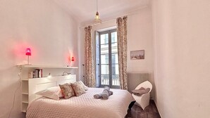 Une chambre à coucher avec un lit, une table de chevet, une lampe et une vue sur la ville par la fenêtre.