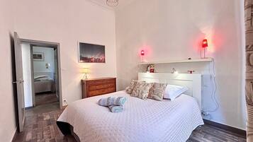 Een slaapkamer met een bed, een dressoir, een nachtkastje, een lamp en een foto aan de muur.