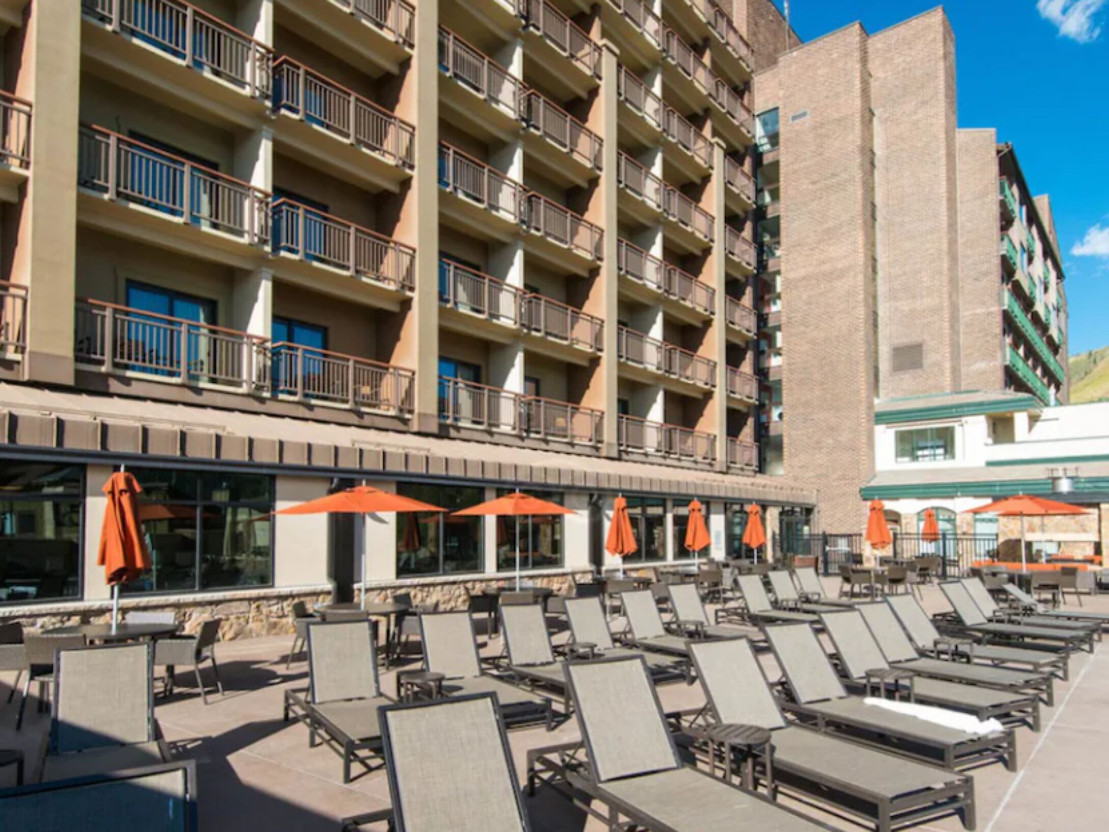 A hotel with multiple floors, outdoor seating with umbrellas, and a pool area with sun loungers.