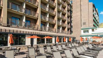 A hotel with multiple floors, outdoor seating with umbrellas, and a pool area with sun loungers.