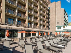 Ein Hotel mit mehreren Etagen, Außenbereich mit Sonnenschirmen und einem Pool mit Liegestühlen.