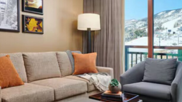 Un salon comprenant un canapé, un fauteuil et une table basse. Les murs sont ornés de tableaux encadrés, et une fenêtre offre une vue sur un paysage enneigé.