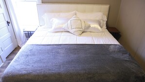 Una cama bien hecha con sábanas blancas y una manta gris.