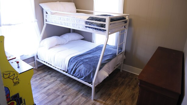 Un lit superposé avec une literie blanche, un plancher en bois et un petit bureau avec une chaise.