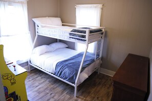Een stapelbed met witte beddengoed, een houten vloer en een klein bureau met stoel.