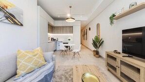 A modern living room with a sofa, a coffee table, a TV, and a dining area with chairs and a table.