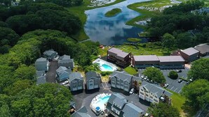 An aerial view of a resort with a central swimming pool, multiple buildings, and a large body of water. - Ogunquit River Outlook (Wells)