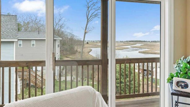 A bedroom with a large window overlooking a river and a wooden deck. - Ogunquit River Outlook (Wells)