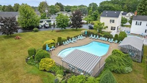 Ein Swimmingpool mit Liegestühlen und einer überdachten Terrasse, umgeben von gepflegten Rasenflächen und Bäumen.