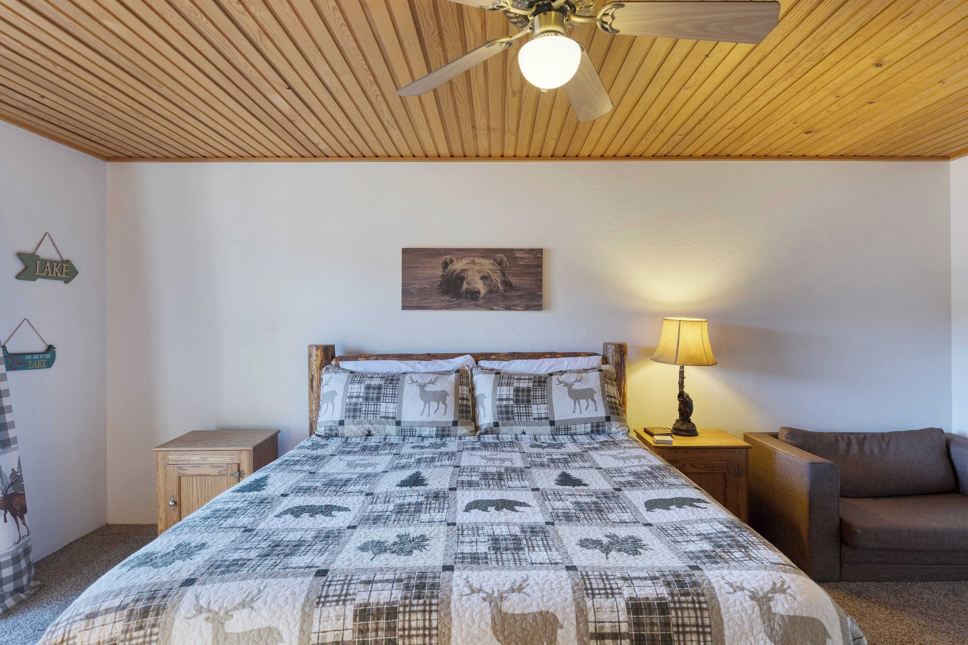 Ein Schlafzimmer mit Holzbalkendecke, einem Bett mit Patchworkdecke mit Tiermotiven, einem Nachttisch mit Lampe und einem an der Wand hängenden Bärenbild.